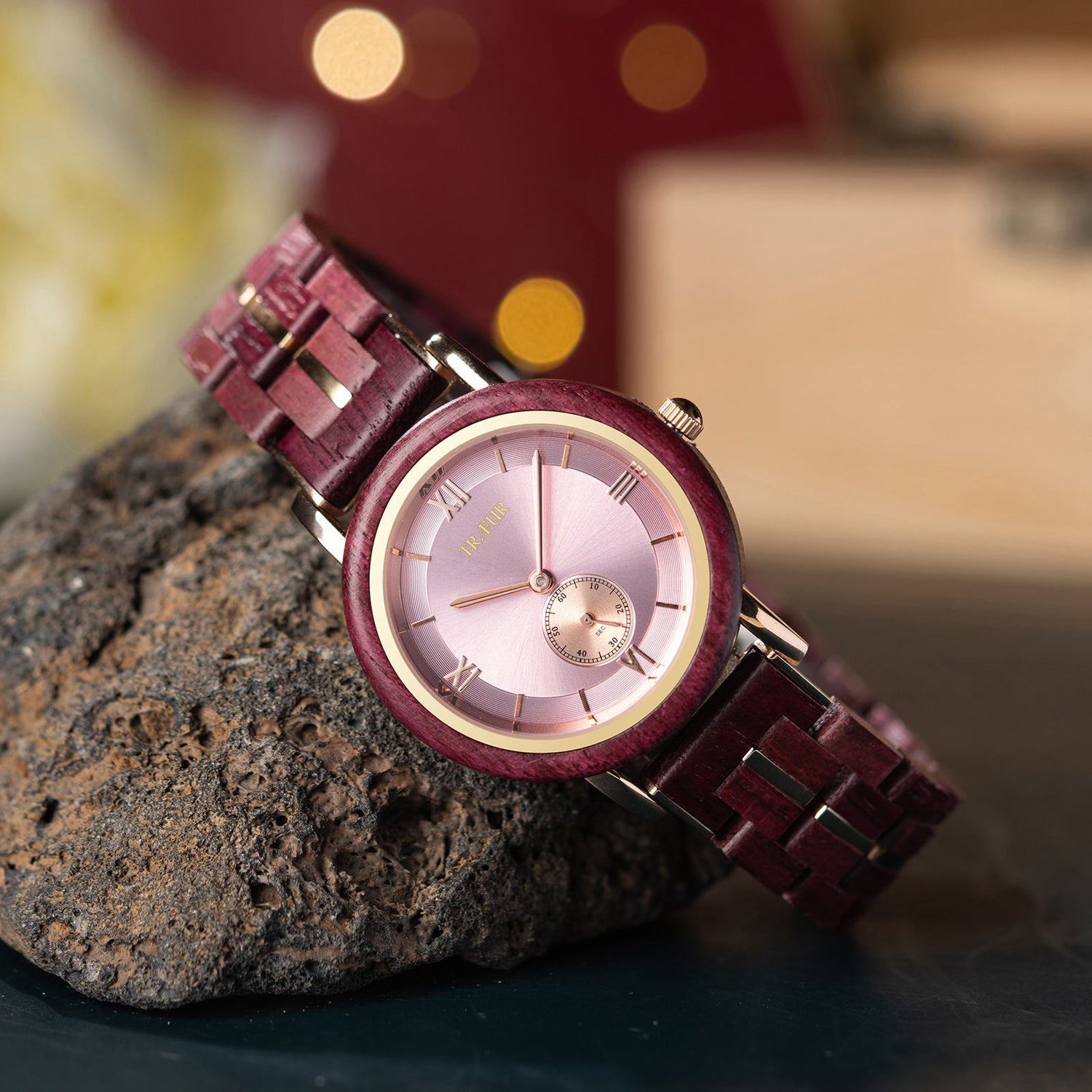 Elegant Trieur wristwatch with purple wooden band and gold-accented pink dial resting on textured rock
