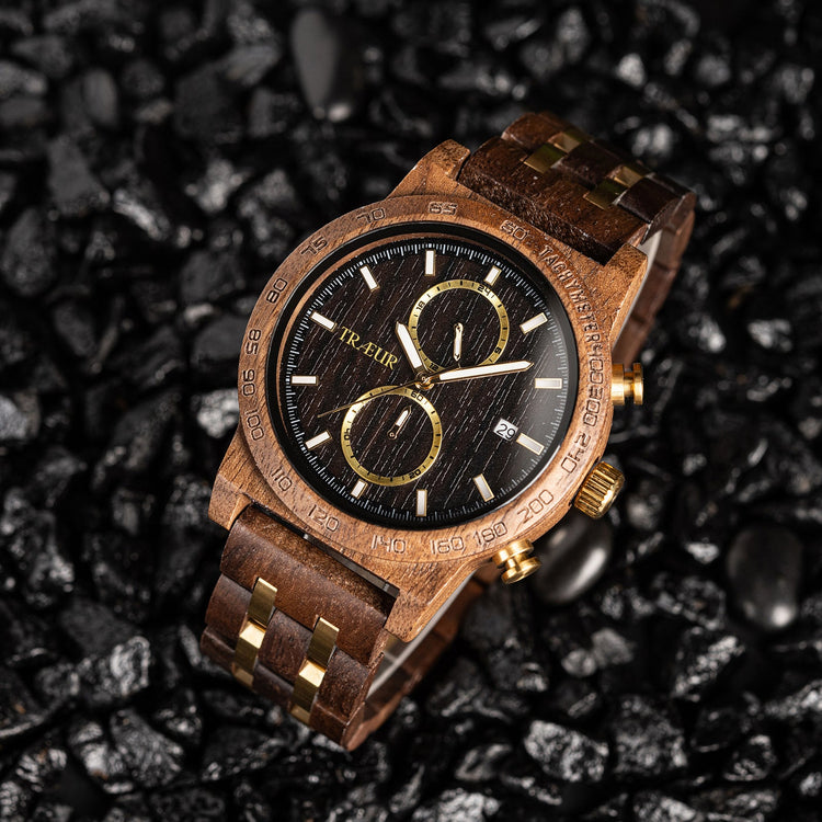 wooden wristwatch with black dial, gold accents, and leather strap on black textured stones