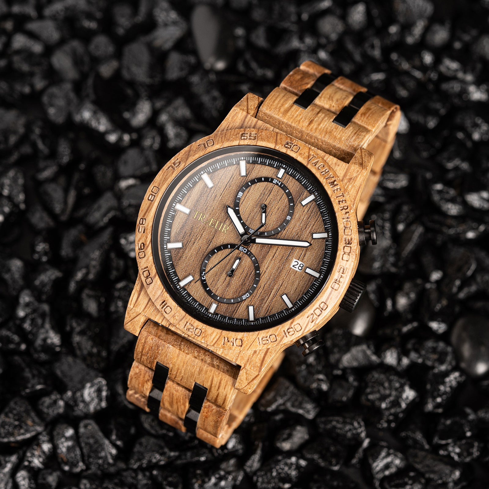 Wooden wristwatch with black accents on dark textured stone background, tachymeter dial