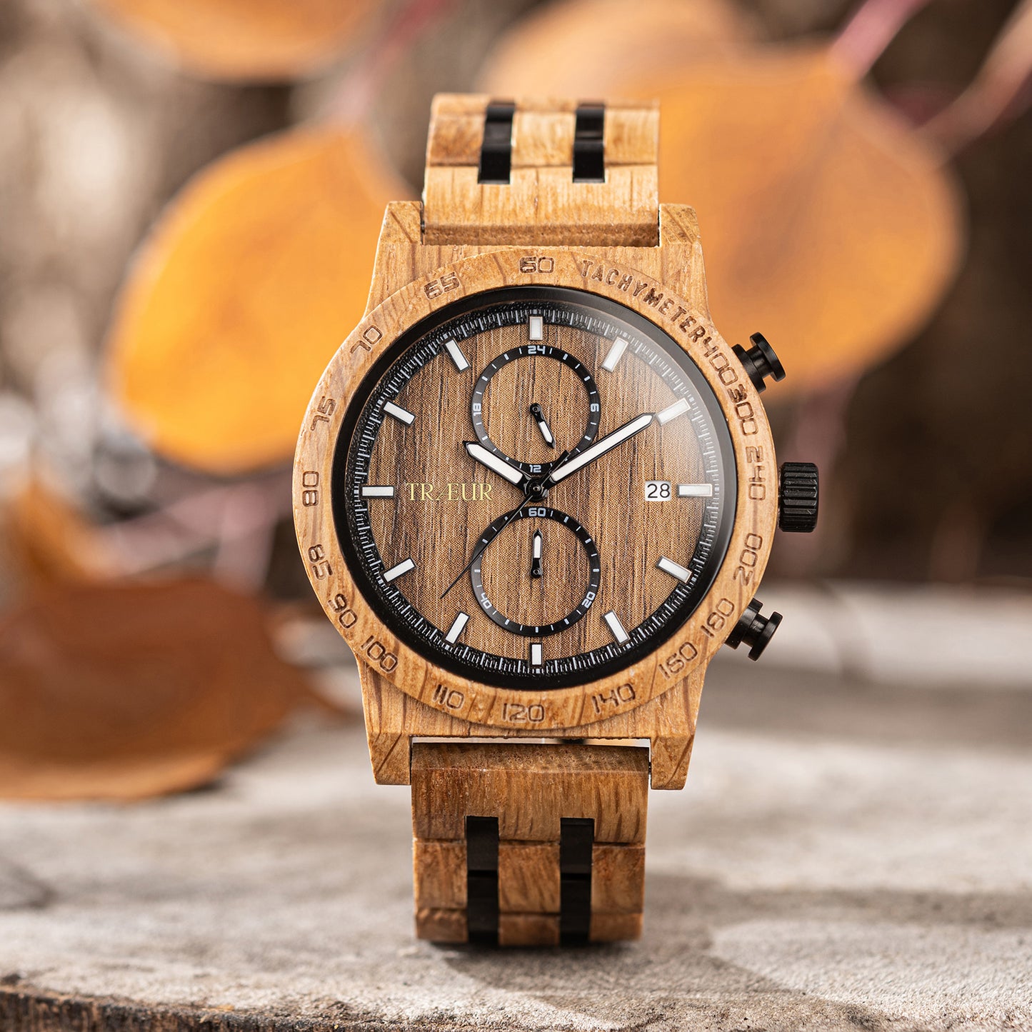 Close-up of a wooden wristwatch with black details and tachymeter bezel on a rustic surface with autumn leaves