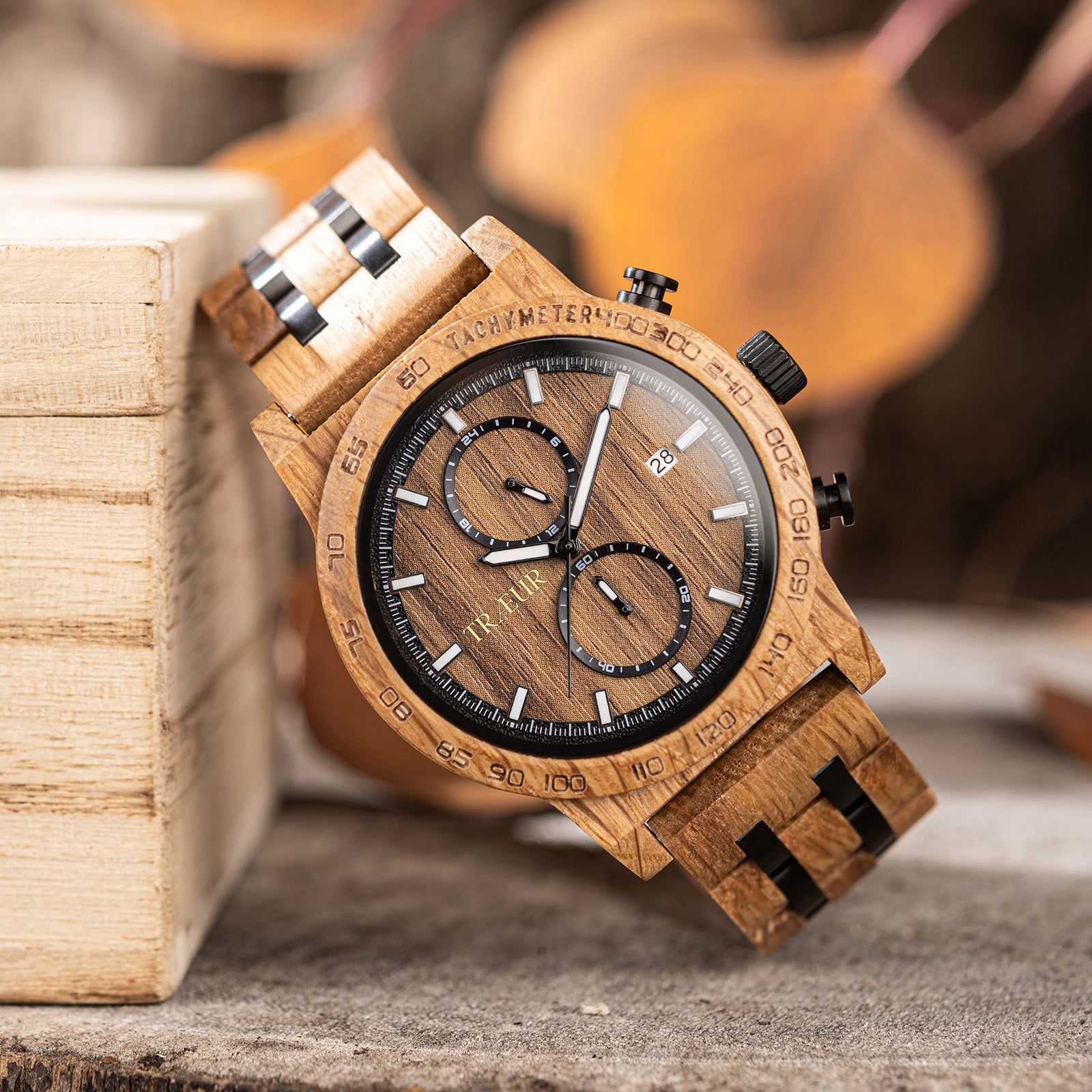 Close-up of wood grain wristwatch with tachymeter, chronograph dials, and date display on wooden surface