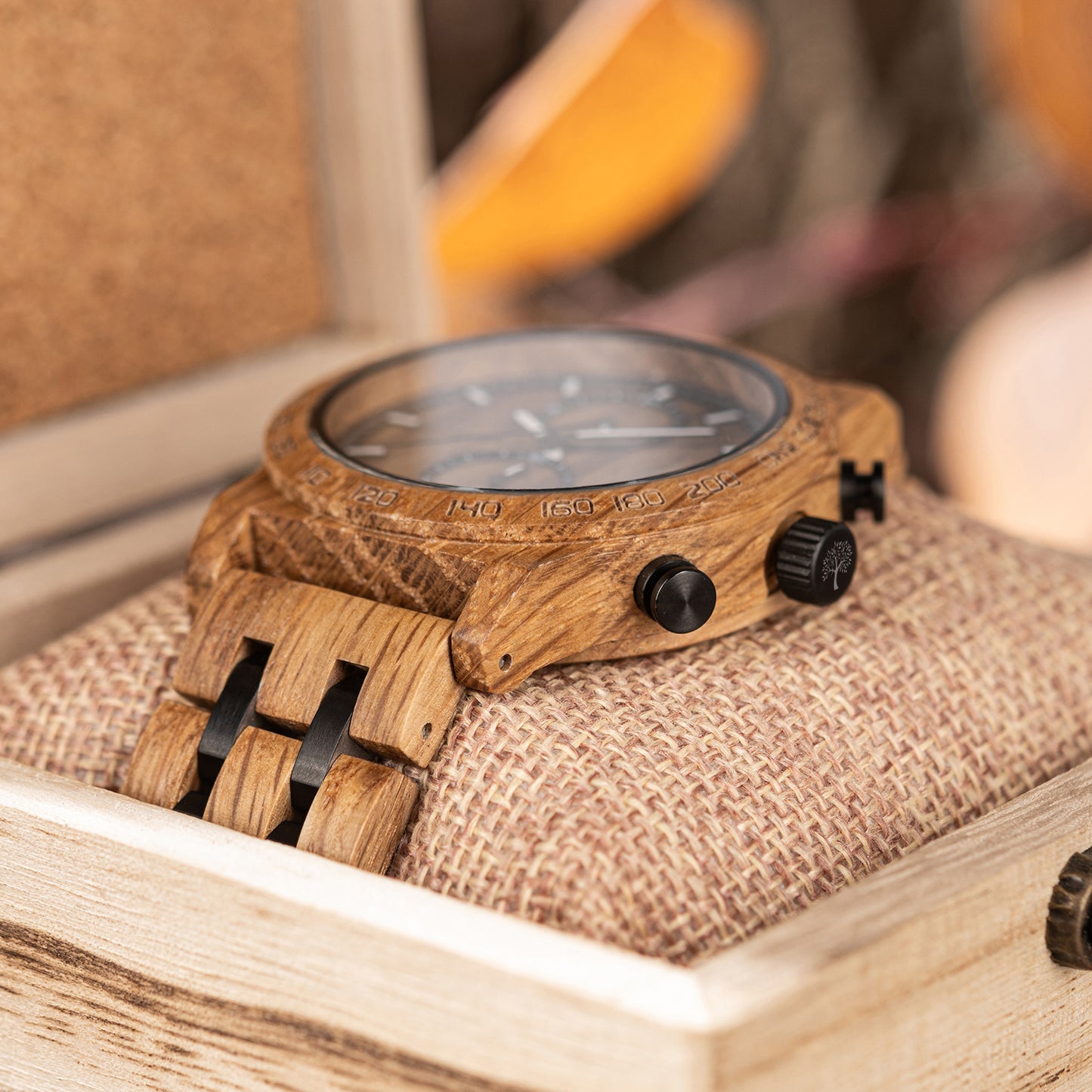 Close-up of wooden wristwatch with black buttons on woven cushion in wooden display box